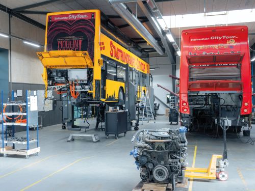 装配车间内停放着两辆敞开后挡板的巴士，其柴油发动机已被取下