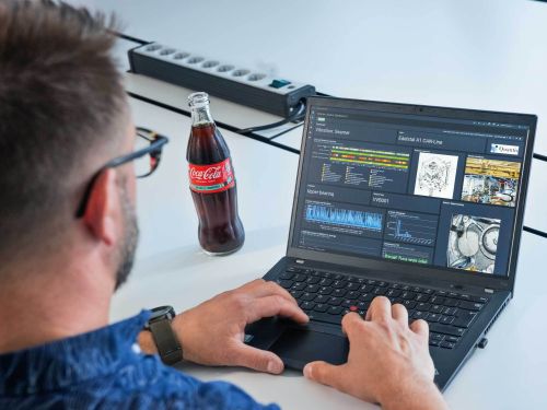 员工看着笔记本电脑，屏幕上是各种图表和工厂的实时图像